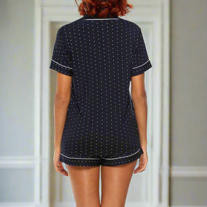 Rear-view of moisture-wicking short sleeve bamboo pj navy polka dot short set with white piping worn by woman with auburn hair. 